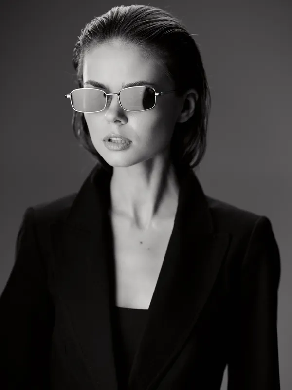 Black and white portrait of stylish woman wearing sunglasses and black blazer with serious expression