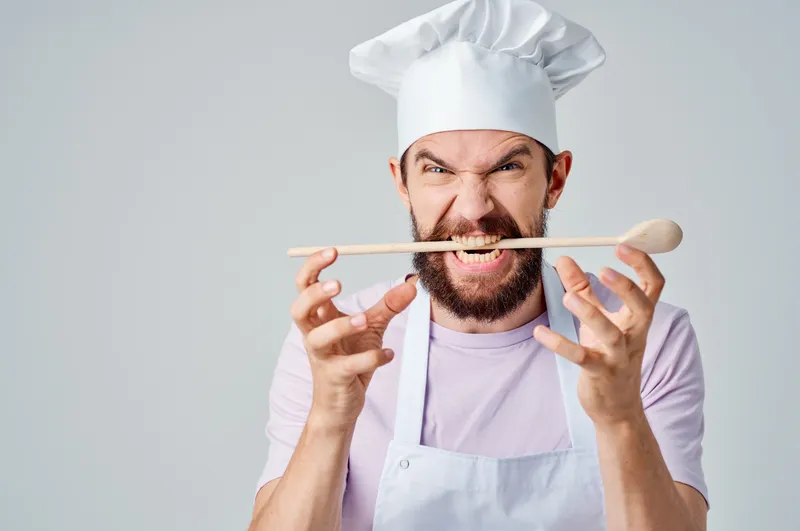 Эмоциональный повар работает на кухне, занимаясь приготовлением пищи