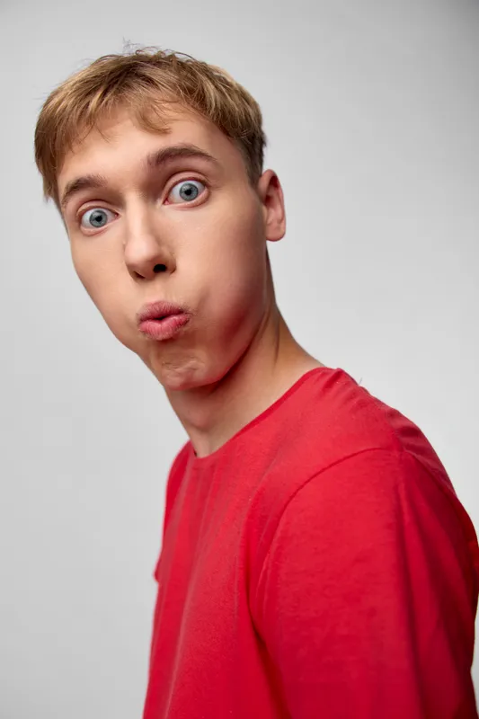 Closeup of a surprised man in a red shirt, capturing a vivid reaction and playful astonishment. Studio lighting highlights facial energy, humor, and a bold, expressive moment.