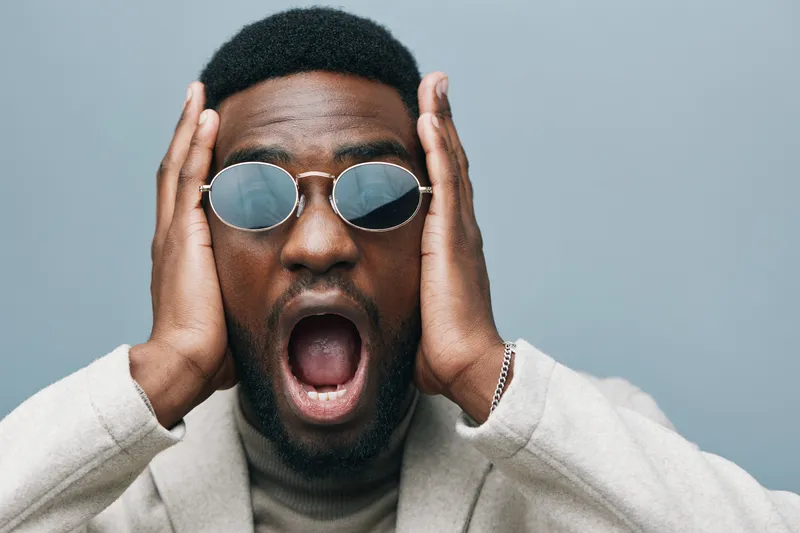Счастливый афроамериканский мужчина в куртке и очках позирует на зеленом фоне