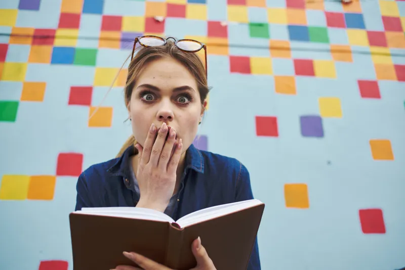 Женщина-студентка с книгой в руке, эмоции, модель и разноцветная стена