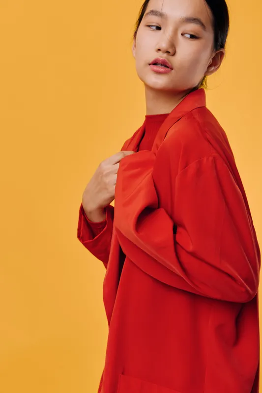 Woman wearing red jacket posing sideways on yellow background with thoughtful expression, fashion style, casual outfit, studio portrait with bright color contrast and modern look.