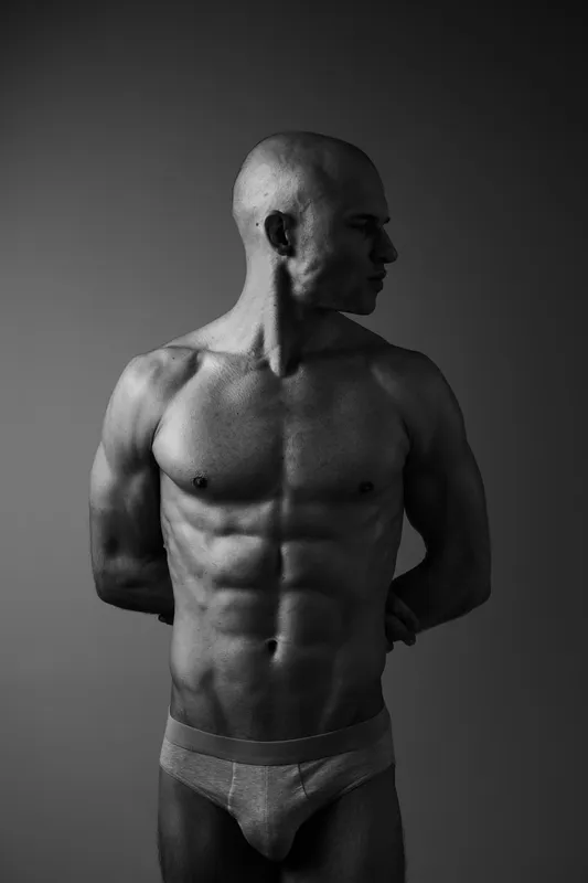 Strong man posing in black and white, showcasing muscular physique with a confident expression and artistic composition. Ideal for fitness and health themes.