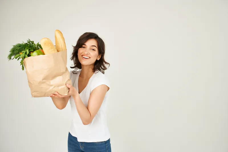 Женщина держит продукты, доставленные из супермаркета, на светлом фоне