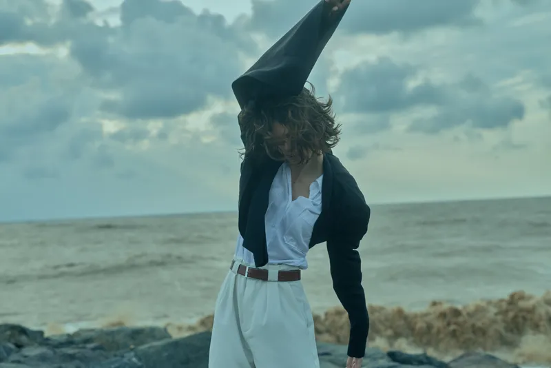 Wizard in a dark blazer and white shirt on a windy beach, tall hat tilted, posing by the shore with moody clouds and waves, fantasy scene for storytelling and cosplay themes