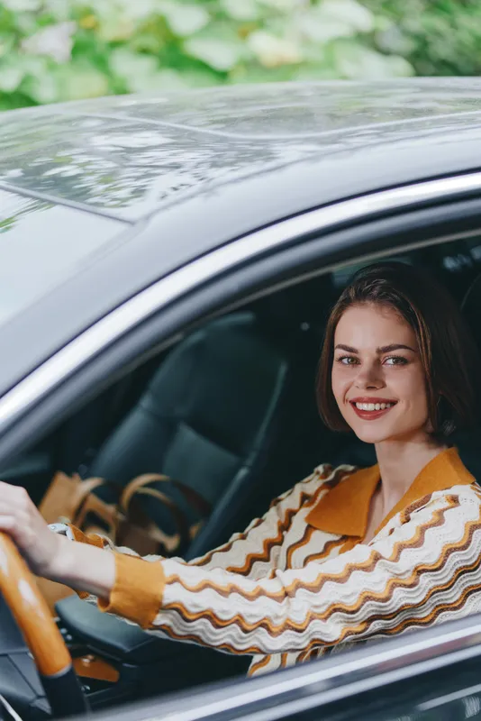 Young woman smiling while driving a car, sitting in the driver's seat with a striped sweater, capturing a confident everyday moment.