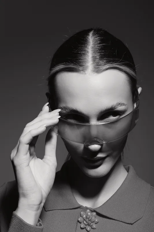 Caucasian woman with light skin wearing futuristic visor sunglasses and stylish outfit looks confidently at camera in black and white portrait studio photo.