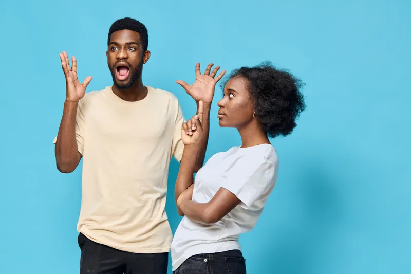 African American couple expressing strong emotions, featuring vibrant blue background, casual attire, and contrasting expressions of surprise and indifference