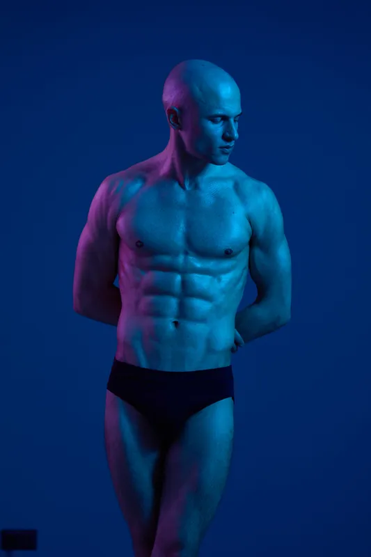 Athletic man posing with confidence in a blue light setting, showcasing a strong physique and an aesthetic presence, perfect for fitness and health concepts.