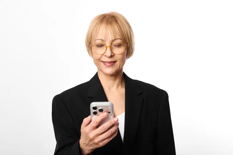 Woman with smartphone and glasses, smiling senior in business suit, portrait on white background, holding phone in hands, calm communication, indoors today