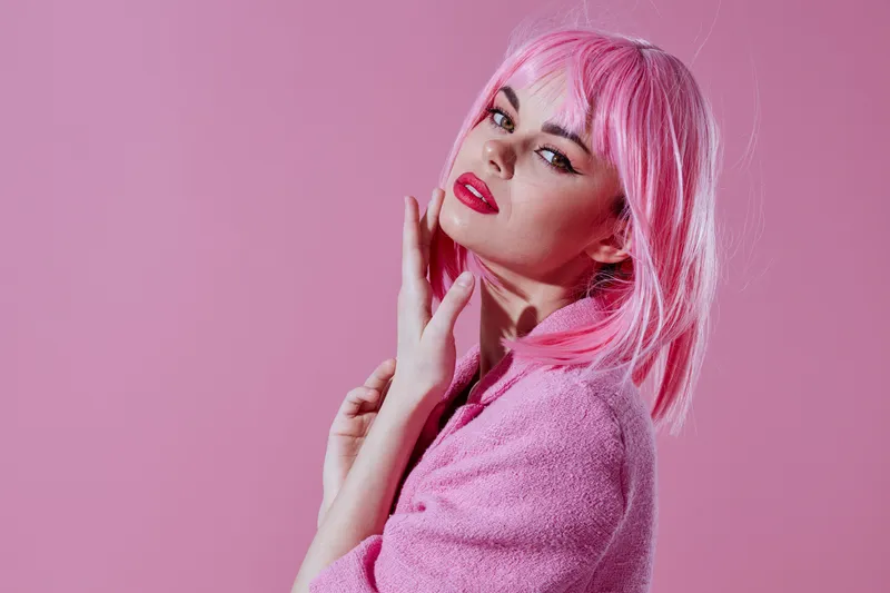 Красивая модная девушка с привлекательным взглядом, в розовом парике и стильной одежде, на розовом фоне