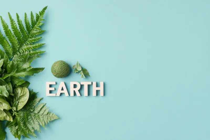 Натюрморт на тему Земли с зеленой листвой, текстурированной сферой и словом EARTH на спокойном голубом фоне