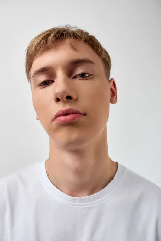 Close up of a young man with a neutral background, wearing a white t shirt, and a relaxed expression, captured in a minimal studio setting for fashion and lifestyle projects