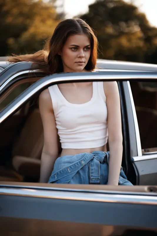Young woman in casual summer outfit leaning on a vintage car, evoking a sense of freedom and adventure in nature.