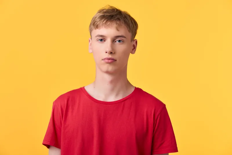 Young man wearing a red shirt stands against a bright yellow background in a clean studio shot, conveying casual style, simplicity and modern fashion for lifestyle content