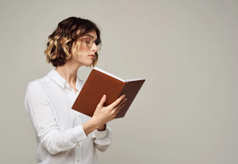 Деловая женщина с книгой в руках на сером фоне, копипространство