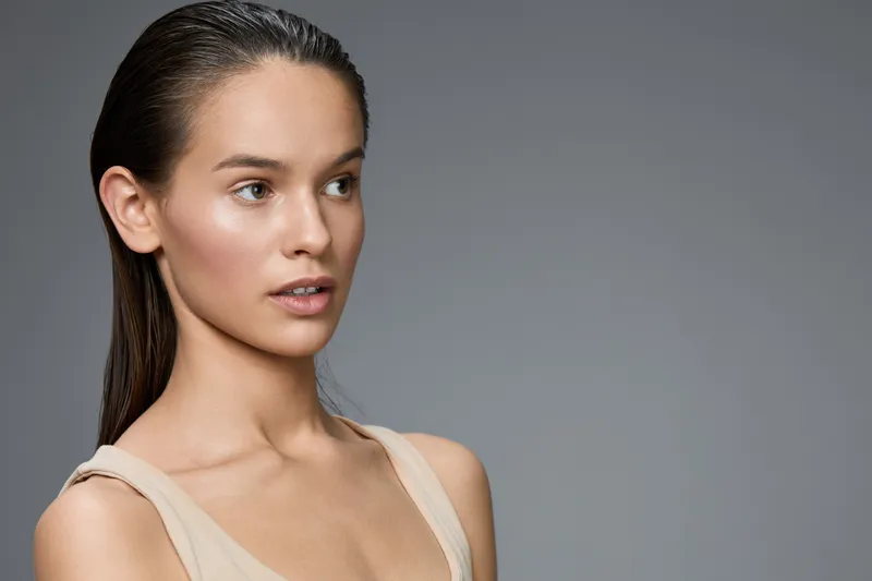 Portrait of a young woman with smooth skin and minimal makeup, showcasing natural beauty against a neutral gray background, ideal for beauty and skincare concepts