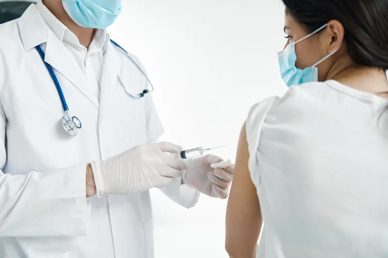 Врач со шприцем в руке делает инъекцию вакцины в защитных перчатках