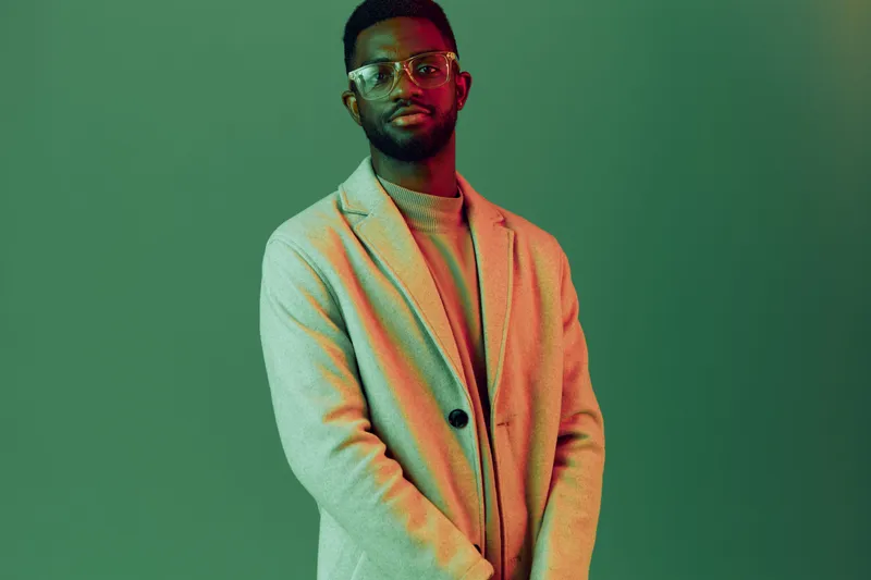 Confident young man in stylish blazer with glasses against a green background, showcasing modern fashion and self assurance