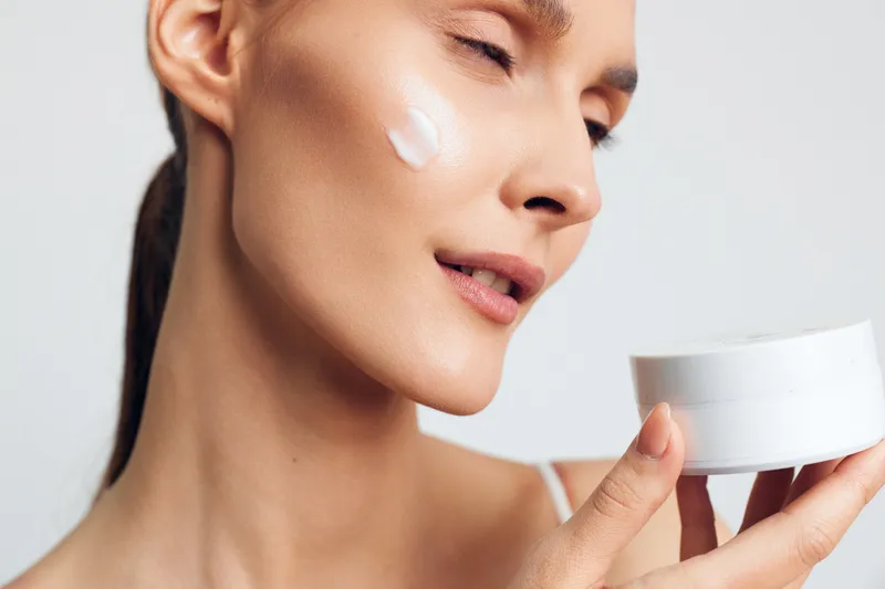 Closeup of woman applying cream on face, skincare routine, natural beauty, smooth skin, relaxed expression, soft lighting, white background, healthy lifestyle concept