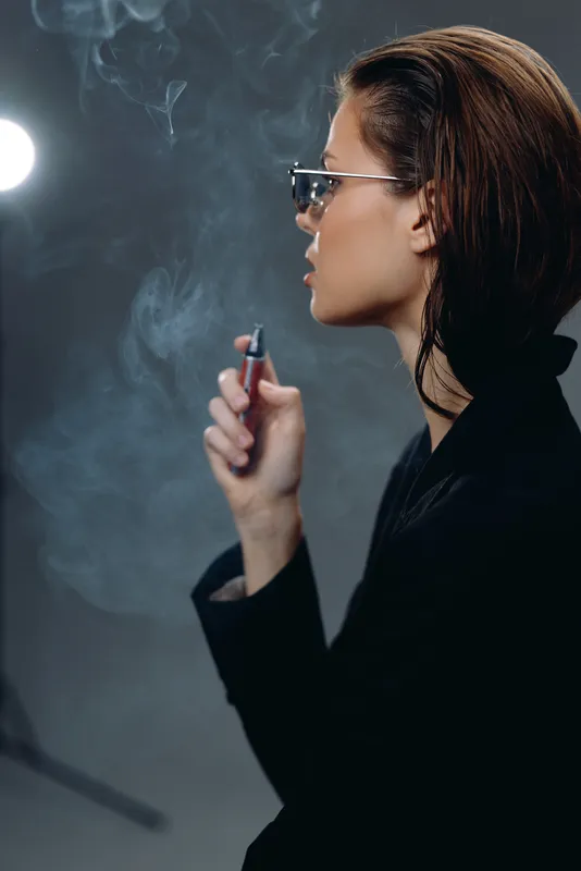 stylish woman smoking electronic cigarette with smoke in dark background