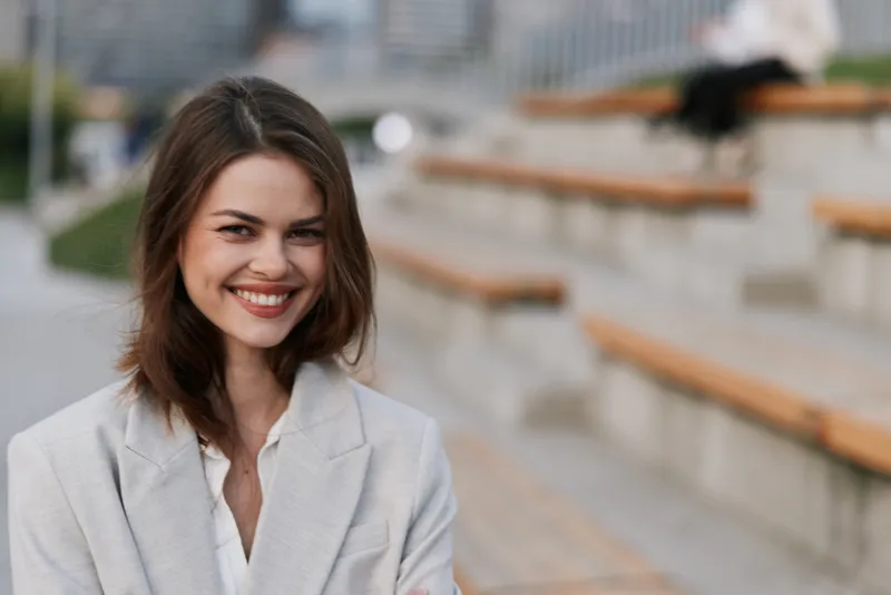 Smiling woman in light gray business suit outdoors with blurred urban background confident and happy professional businesswoman