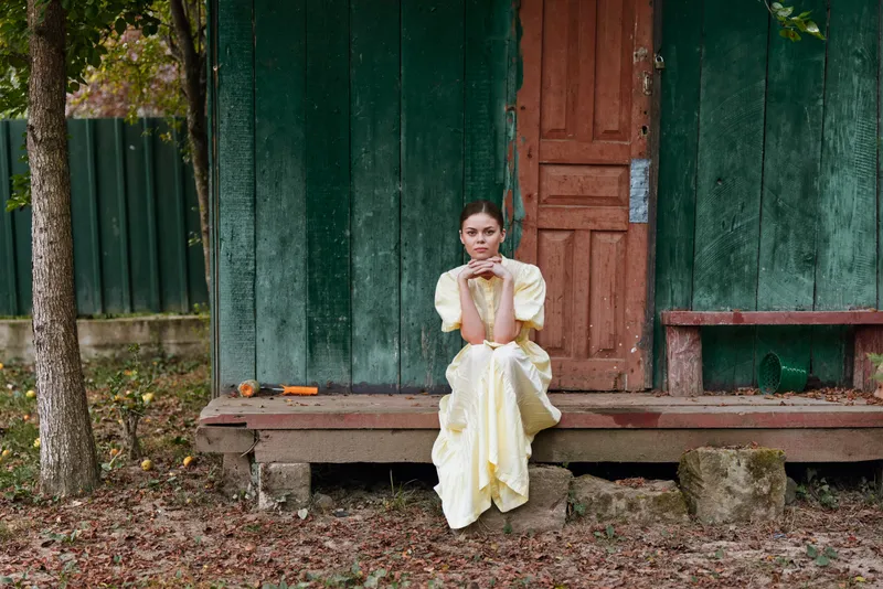 Woman on porch in yellow dress rustic countryside sitting contemplative among autumn leaves authenticity inclusivity