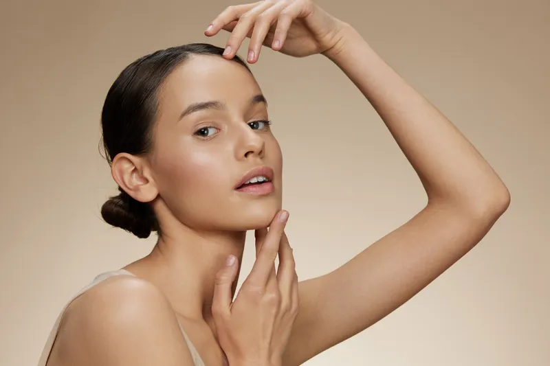 Elegant portrait of a young woman with neutral makeup showcasing natural beauty against a soft beige background, representing skincare and self care concepts