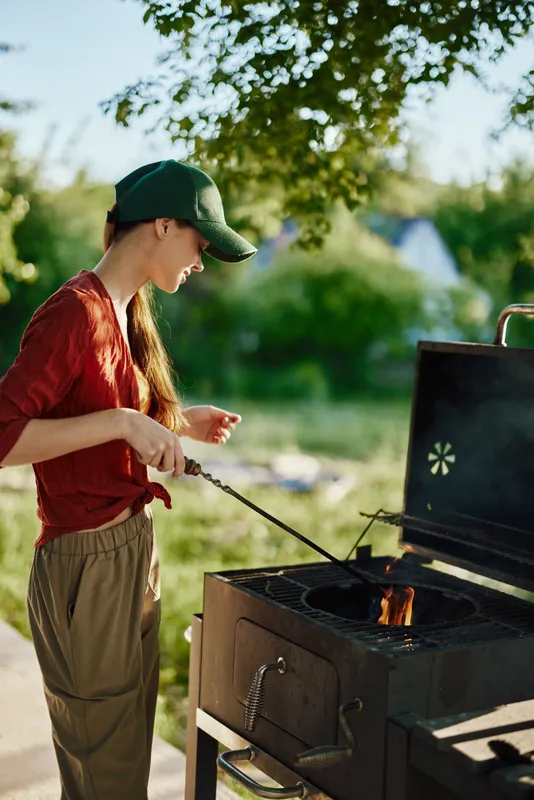 Young woman grilling outdoors in a relaxed summer setting, showcasing joy and connection to nature with vibrant green background, perfect for seasonal barbecue ideas