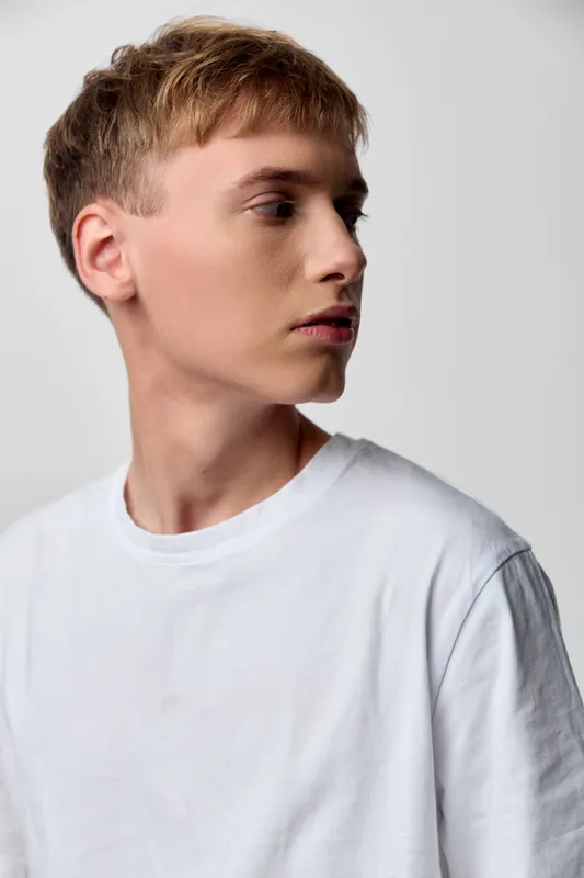 Man in a white t shirt in profile, casual fashion, looking away with a minimal lean silhouette, studio light and calm modern pose for fashion and lifestyle