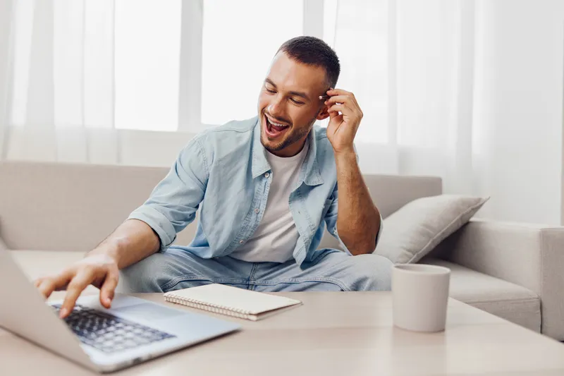 Happy man engaging with his laptop at home, showcasing creativity and productivity. Bright interior enhances the positive atmosphere and inspiration.