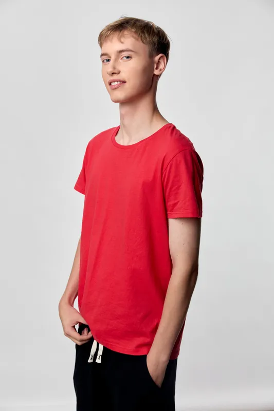Young man in a red shirt stands in a studio, casual wear with a relaxed pose against a plain background, clean lighting, fashion focused and ideal for lifestyle apparel campaigns