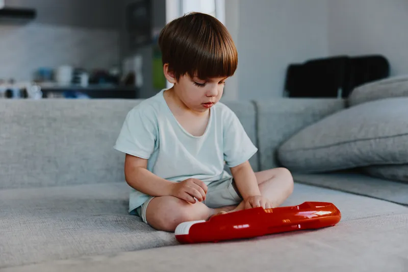 Focused boy playing with a toy piano, showcasing creativity and concentration in a cozy living room, surrounded by soft textures and warm colors.