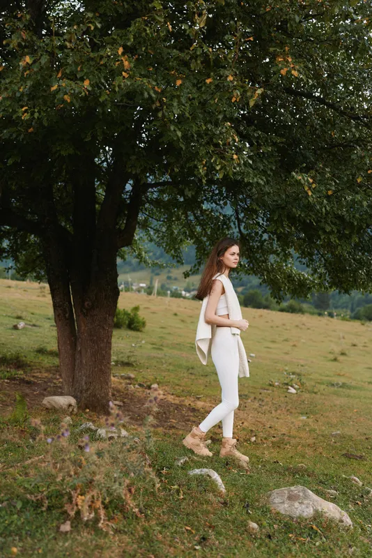 Relaxed woman strolling through a sunlit countryside, dressed in white, enjoying fresh air and nature, a casual lifestyle moment by a large tree.