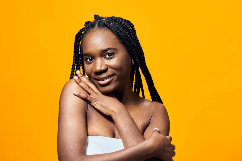 Young Black woman with braided hair smiling against a vibrant yellow background, showcasing confidence and beauty in a modern portrait style