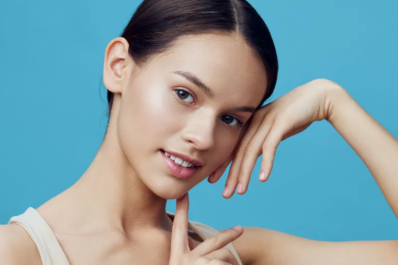 Young woman with natural beauty expression on a blue background, showcasing healthy skin, confidence, and simplicity in casual attire
