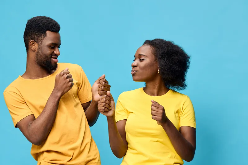 Happy couple dancing together in matching yellow outfits against a vibrant blue backdrop, expressing joy and connection through movement and laughter