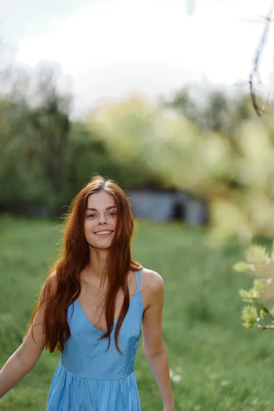 Женщина улыбается, обнажая зубы, весной в солнечный день, счастливо гуляя на природе на фоне зеленой травы