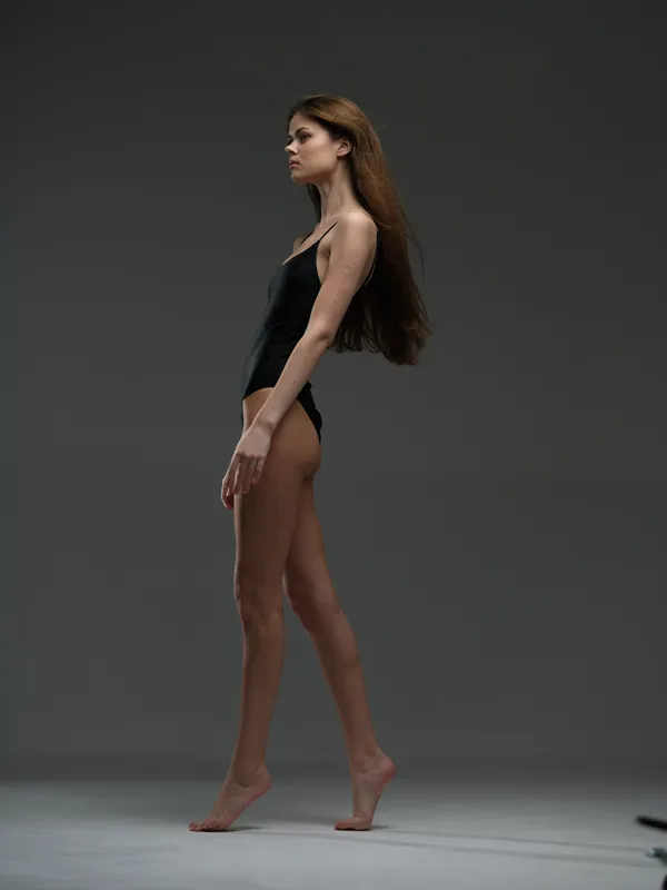 slender woman in black bodysuit standing on gray background with soft studio lighting