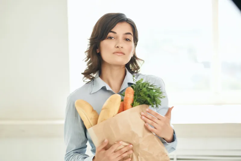 Женщина в семейной одежде держит пакет с продуктами здорового питания и делает домашнюю работу