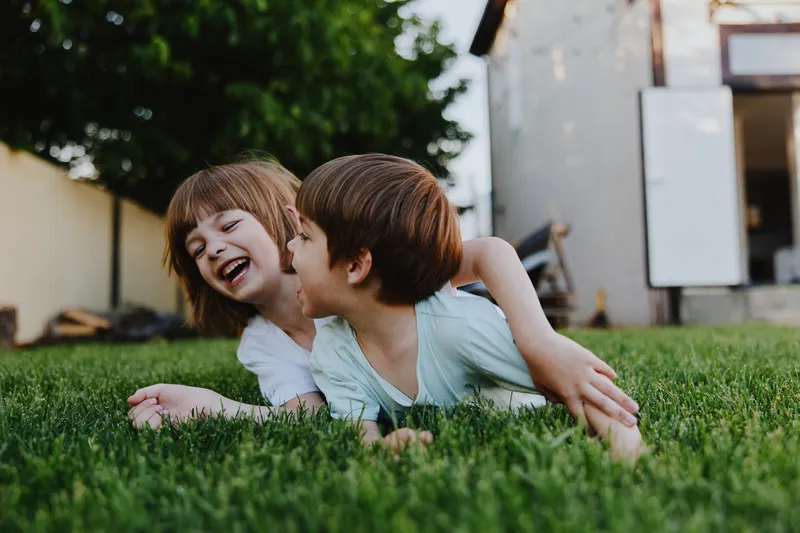 Laughing children playing in a grassy yard, showcasing joy and innocence in a bright and cheerful atmosphere with warm sunlight illuminating the scene.