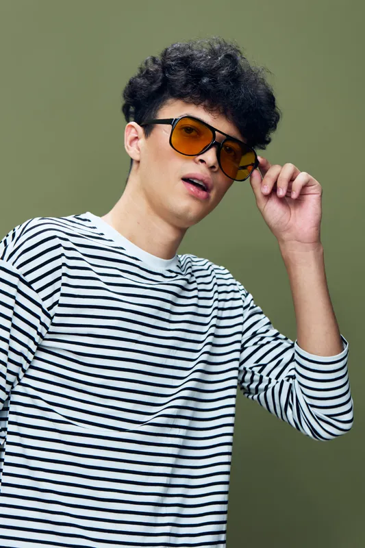 young man with sunglasses wearing striped shirt posing against olive background, casual style, trendy look, confident expression, modern fashion portrait