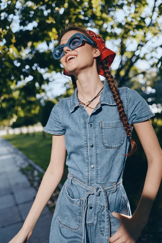 lifestyle woman in modern boho-western denim dress with sunglasses and braided hair enjoying sunny street style in vibrant film color tones