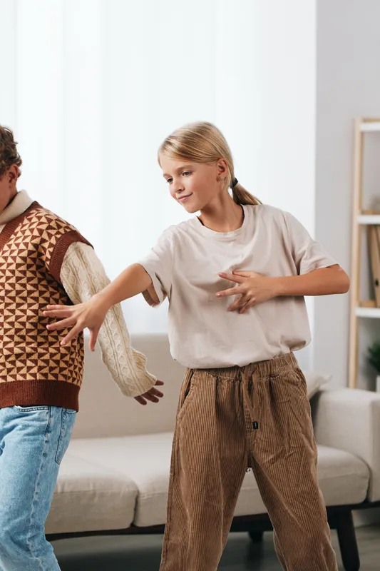 Authentic depiction of playful energy in a home setting, featuring school-aged youth dancing with genuine expression, showcasing casual fashion and everyday lifestyle.