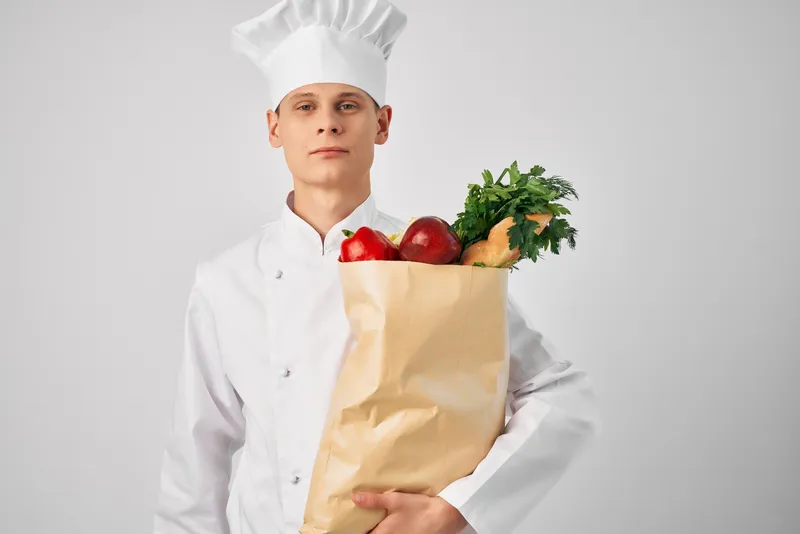 Мужчина в поварской форме с пакетом продуктов работает на кухне ресторана