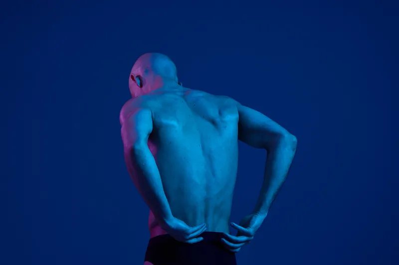 Artistic portrayal of a male swimmer's back, showcasing a strong build and athleticism under vibrant blue lighting. The image captures a sense of determination and focus.