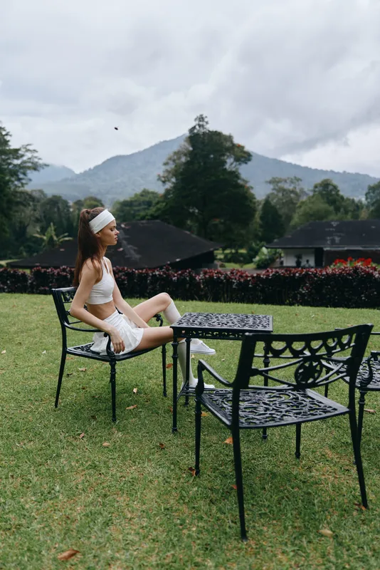 Young woman in sportswear sitting on a garden chair, enjoying a peaceful moment in nature, with a serene landscape in the background on a cloudy day