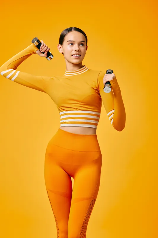 Vibrant scene of a woman in orange athletic wear lifting dumbbells, showcasing fitness, strength and active lifestyle in a bold studio portrait.