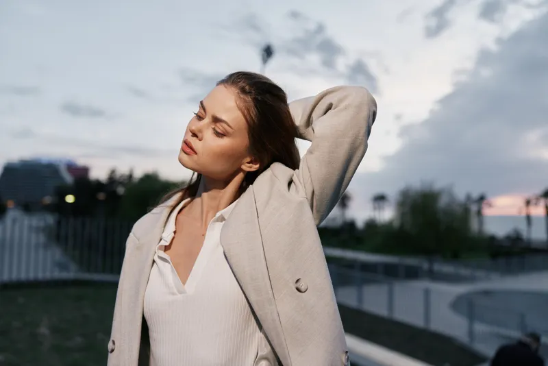 woman in beige coat expressing calmness outdoors at sunset with soft natural light sky background urban fashion style