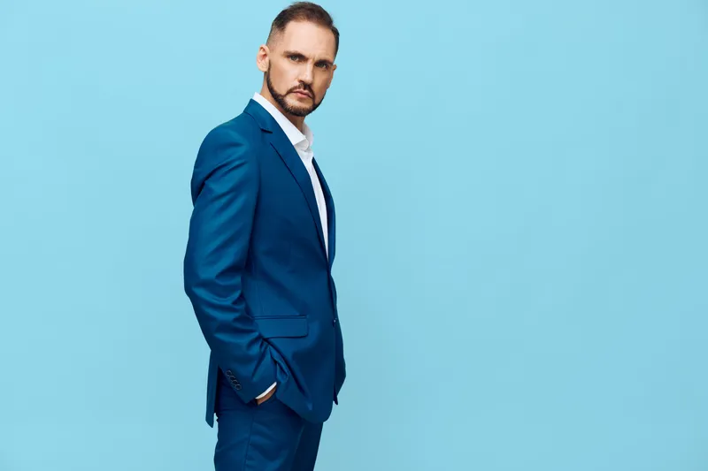 A professional businessman in a blue suit stands against a solid blue backdrop, an isolated color scene that highlights confidence, focus, and poised leadership.